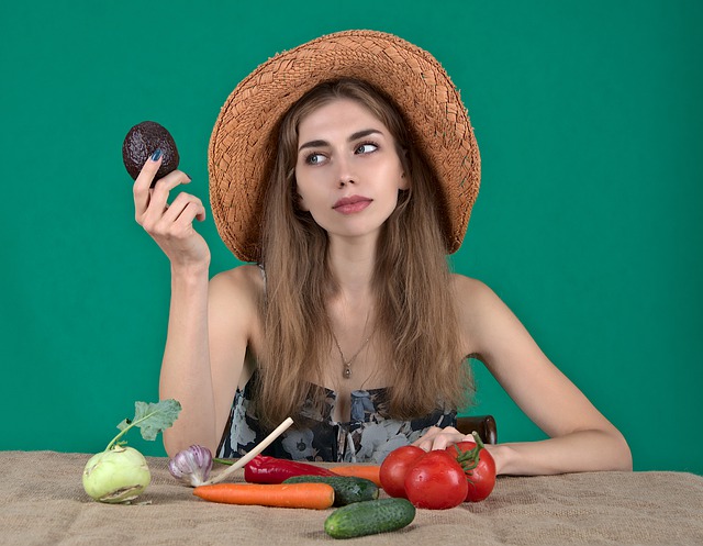 Dievča v slamenom klobúku sedí za stolom, na ktorom je ovocie a zelenina